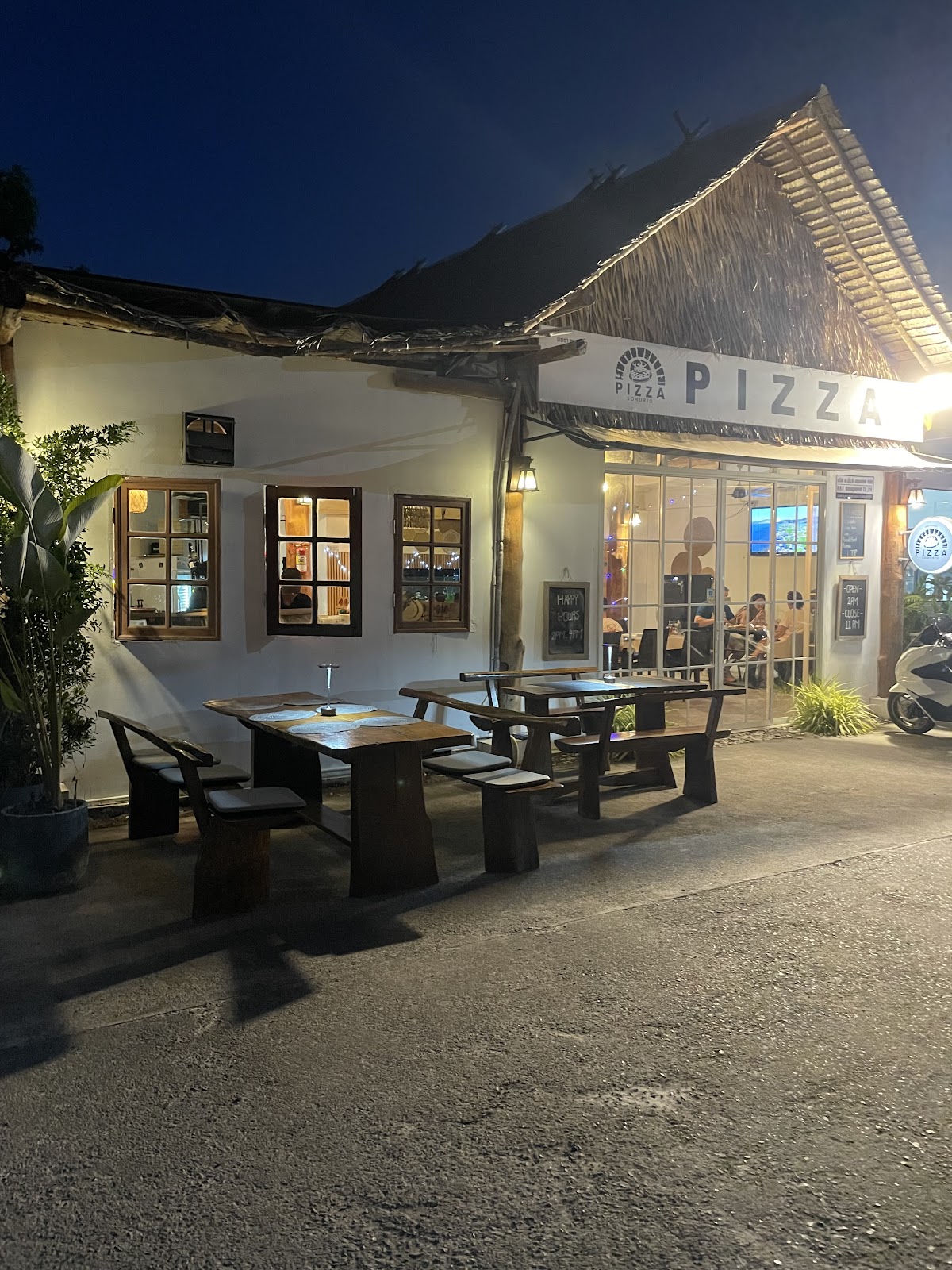 Pizza Sondrio exterior at night with thatched roof